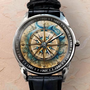 May include: A silver wristwatch with a black leather band. The watch face features a detailed compass design with gold and blue accents, surrounded by a black bezel with white numerals. The design includes nautical elements.