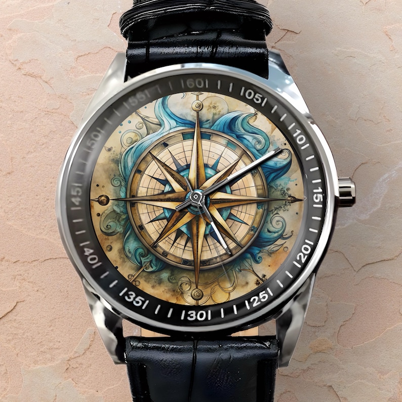 May include: A silver wristwatch with a black leather band. The watch face features a detailed compass design with gold and blue accents, surrounded by a black bezel with white numerals. The design includes nautical elements.