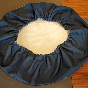 May include: A dark blue round fabric cover with a white lining. The cover is gathered at the top and bottom, creating a ruffled effect.