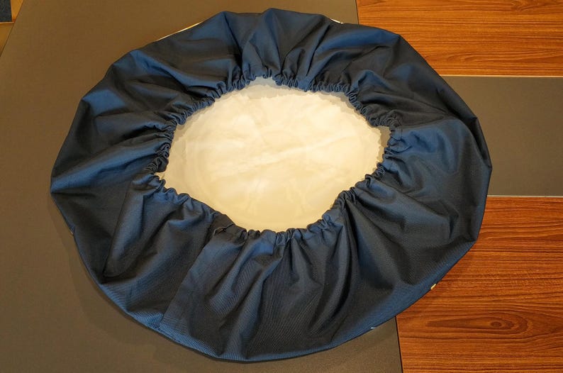 May include: A dark blue round fabric cover with a white lining. The cover is gathered at the top and bottom, creating a ruffled effect.