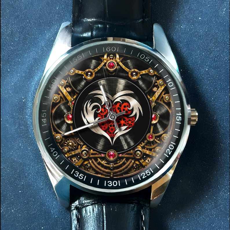 May include: A wristwatch with a black leather strap and a silver-tone metal case. The watch face features a complex mechanical gear design in gold and black, centered around a stylized white heart shape filled with small red gears and red accents.