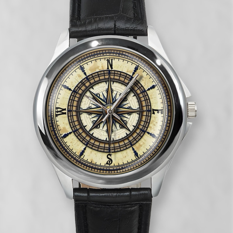 May include: A silver wristwatch with a black leather band. The watch face features a compass design with a cream-colored background, black and gold detailing, and a second hand.