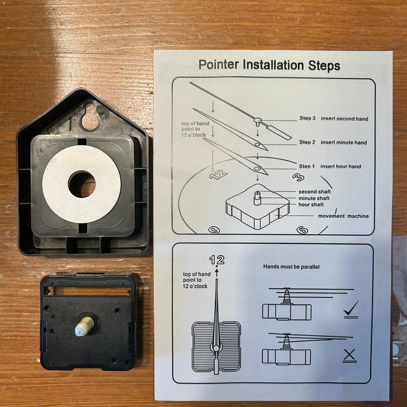 May include: Clock parts, including a black clock movement, a black housing, and a paper with pointer installation steps. The paper shows how to install the hour, minute, and second hands. The text on the paper says "Pointer Installation Steps."