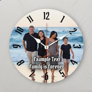 Peut inclure: Horloge murale ronde avec une photo de famille sur le cadran, des chiffres et des aiguilles noirs. Le cadran de l'horloge comprend le texte "Example Text Family is forever". L'arrière-plan montre une famille à la plage.