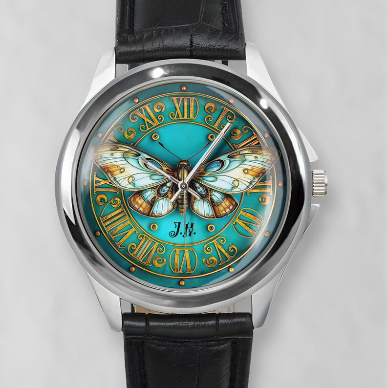 May include: A silver wristwatch with a black leather band. The watch face features a teal background with a butterfly design and gold Roman numerals. The initials "J.H." are at the bottom.