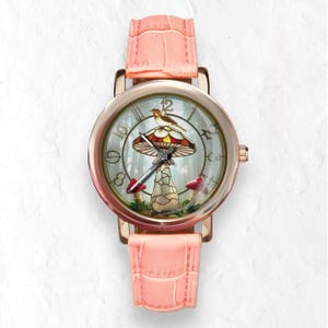 Puede incluir: Un reloj de pulsera de oro rosa con una correa de cuero rosa claro. La esfera del reloj presenta un dise&ntilde;o caprichoso de hongo con un p&aacute;jaro posado encima. El fondo muestra una escena de bosque con setas rojas.