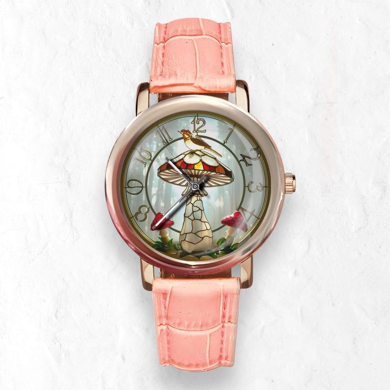Puede incluir: Un reloj de pulsera de oro rosa con una correa de cuero rosa claro. La esfera del reloj presenta un dise&ntilde;o caprichoso de hongo con un p&aacute;jaro posado encima. El fondo muestra una escena de bosque con setas rojas.