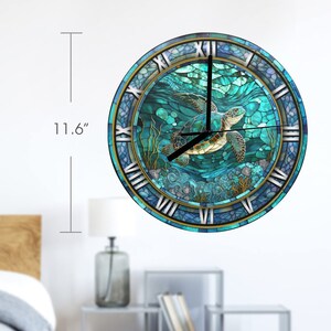 May include: Round wall clock with a sea turtle design. The clock face is 29.5 cm in diameter, with a blue and teal stained glass effect. Roman numerals mark the hours, and the clock hands are black.