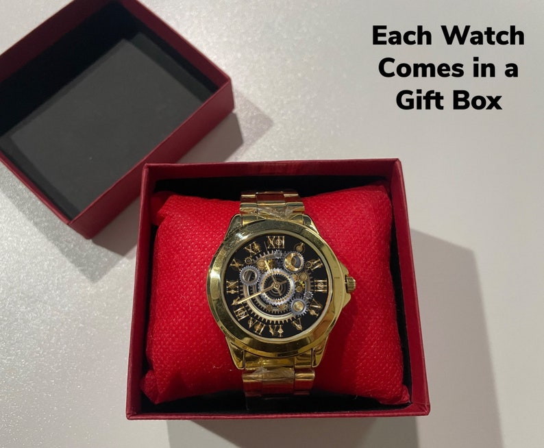 K&ouml;nnte beinhalten: Eine goldfarbene Uhr mit einem Skelettzifferblatt und r&ouml;mischen Ziffern als Stundenmarkierungen. Die Uhr befindet sich in einer roten Geschenkbox. Jede Uhr wird in einer Geschenkbox geliefert.