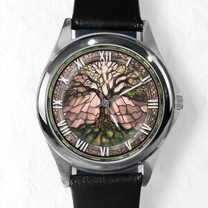 May include: A silver wristwatch with a black leather band. The watch face features a detailed tree design in shades of brown, green, and pink, with Roman numeral hour markers. The watch has a stainless steel case.