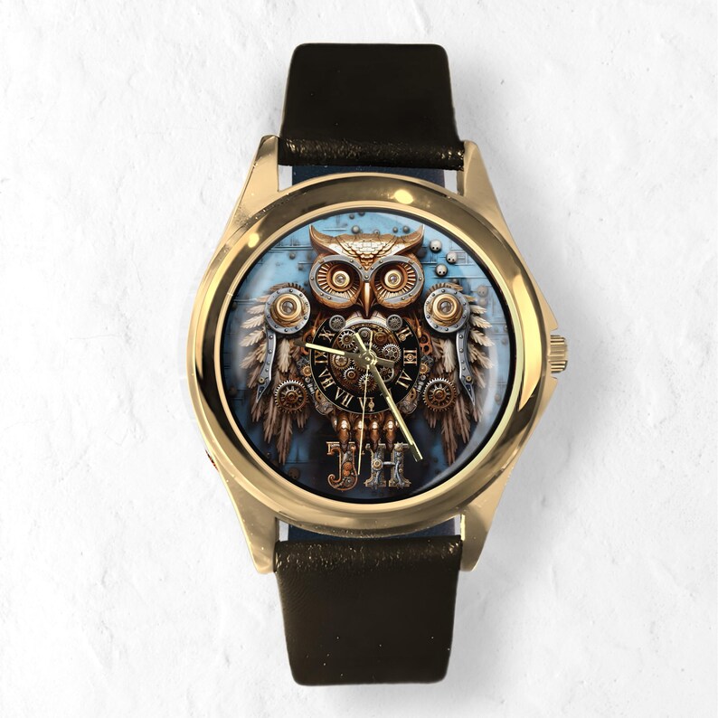 K&ouml;nnte beinhalten: Goldfarbene Armbanduhr mit schwarzem Lederarmband. Das Zifferblatt zeigt ein detailliertes Steampunk-Eulen-Design mit Zahnr&auml;dern, r&ouml;mischen Ziffern und den Initialen "JH". Der Hintergrund ist ein hellblaues Holzmaserungsmuster.