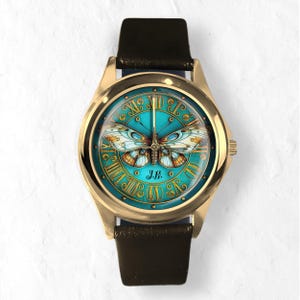 May include: Gold-tone wristwatch with a teal face featuring a butterfly design. The watch face has Roman numerals and the initials "J.H." The watch has a black leather band.