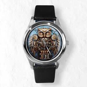 K&ouml;nnte beinhalten: Eine silberne Armbanduhr mit schwarzem Lederarmband. Das Zifferblatt zeigt ein detailliertes Steampunk-Eulen-Design mit Zahnr&auml;dern, Fl&uuml;geln und r&ouml;mischen Ziffern. Die Eule ist in Gold-, Braun- und Blaut&ouml;nen gehalten.