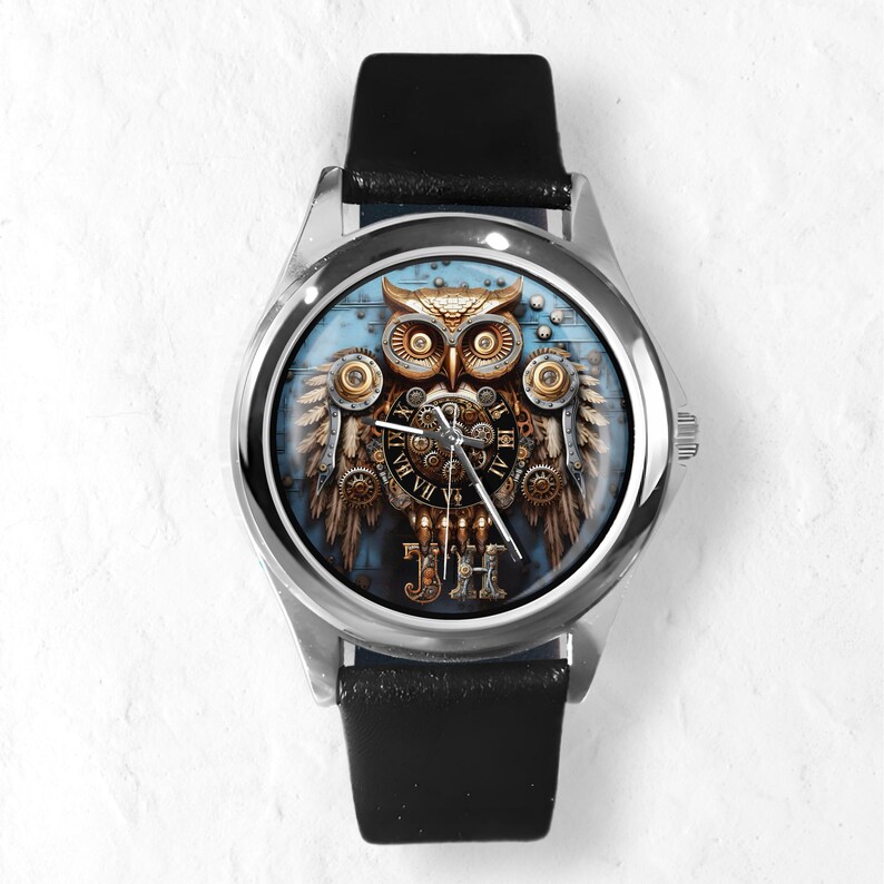 K&ouml;nnte beinhalten: Eine silberne Armbanduhr mit schwarzem Lederarmband. Das Zifferblatt zeigt ein detailliertes Steampunk-Eulen-Design mit Zahnr&auml;dern, Fl&uuml;geln und r&ouml;mischen Ziffern. Die Eule ist in Gold-, Braun- und Blaut&ouml;nen gehalten.
