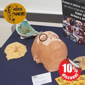 Può includere: Un primo piano di un calco in gesso di un viso con una benda nera sull'occhio. Il calco è su una superficie blu con un cartello che dice "Non Toccare (significa non toccare)". C'è un cartello di sconto del 10% nell'angolo in basso a destra dell'immagine.