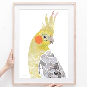 Puede incluir: Una impresi&oacute;n art&iacute;stica enmarcada con una ilustraci&oacute;n de acuarela de una cacat&uacute;a ninfa. El ave tiene plumaje amarillo, gris y naranja con patrones intrincados. La obra de arte est&aacute; sobre un fondo blanco y el marco es de madera clara.