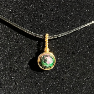 May include: A gold chain necklace with a round pendant featuring a green and pink gemstone.