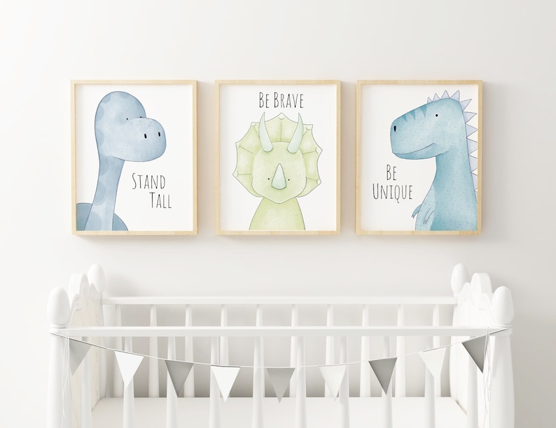 May include: Three framed wall art prints featuring watercolor dinosaurs. The left print shows a blue long-necked dinosaur with the text Stand Tall. The center print shows a green triceratops with the text Be Brave. The right print shows a blue dinosaur with the text Be Unique.