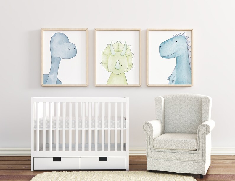 May include: Three watercolor dinosaur prints in light blue, green, and yellow colors. The prints are framed in natural wood and hung on a white wall above a white crib and a white armchair.