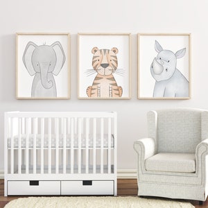 Puede incluir: Tres impresiones art&iacute;sticas enmarcadas de animales: un elefante, un tigre y un rinoceronte. El elefante es gris, el tigre es naranja y marr&oacute;n, y el rinoceronte es gris. Las impresiones est&aacute;n sobre una cuna blanca y un sill&oacute;n gris, creando un tema de guarder&iacute;a.
