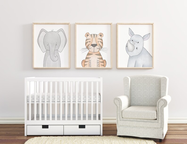 Puede incluir: Tres impresiones art&iacute;sticas enmarcadas de animales: un elefante, un tigre y un rinoceronte. El elefante es gris, el tigre es naranja y marr&oacute;n, y el rinoceronte es gris. Las impresiones est&aacute;n sobre una cuna blanca y un sill&oacute;n gris, creando un tema de guarder&iacute;a.