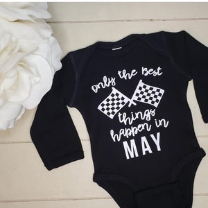 May include: Black long-sleeved baby bodysuit with white text and checkered flags. The text reads "only the best things happen in MAY". The bodysuit is made of soft fabric and is designed for infants.