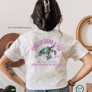 May include: White t-shirt with a purple and green design featuring a sea turtle and the text "Epsilon Sigma Alpha 19 29 The Wild Within Always an Adventure with ESA"
