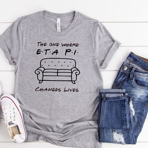 May include: Gray t-shirt with a black graphic of a couch and the text "The One Where E.T.A. P.I. Changes Lives".