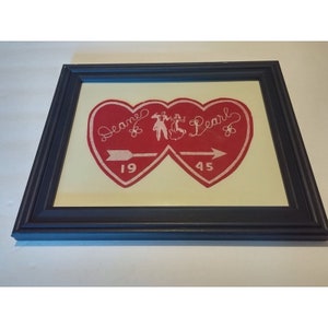 May include: A framed red heart-shaped piece of fabric with the words "Seane & Pearl" and the numbers "19" and "45" embroidered on it. The hearts are joined by a white silhouette of a couple dancing.