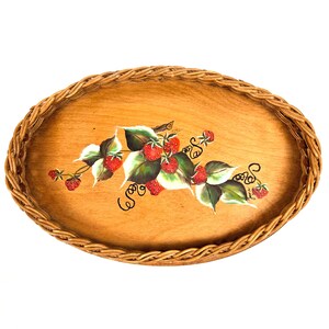 Könnte beinhalten: Ovale Serviertablett aus Holz mit einem gewebten Weidenrand. Das Tablett zeigt ein handgemaltes Design aus roten Erdbeeren, grünen Blättern und schwarzen, lockigen Ranken. Die Holzoberfläche hat eine hellbraune Farbe.