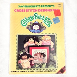 May include: A vintage Cabbage Patch Kids cross stitch design book. The cover features the Cabbage Patch Kids logo, dolls, and a framed cross-stitch design. The book is titled "Xavier Roberts Presents Cross Stitch Designs for Cabbage Patch Kids."