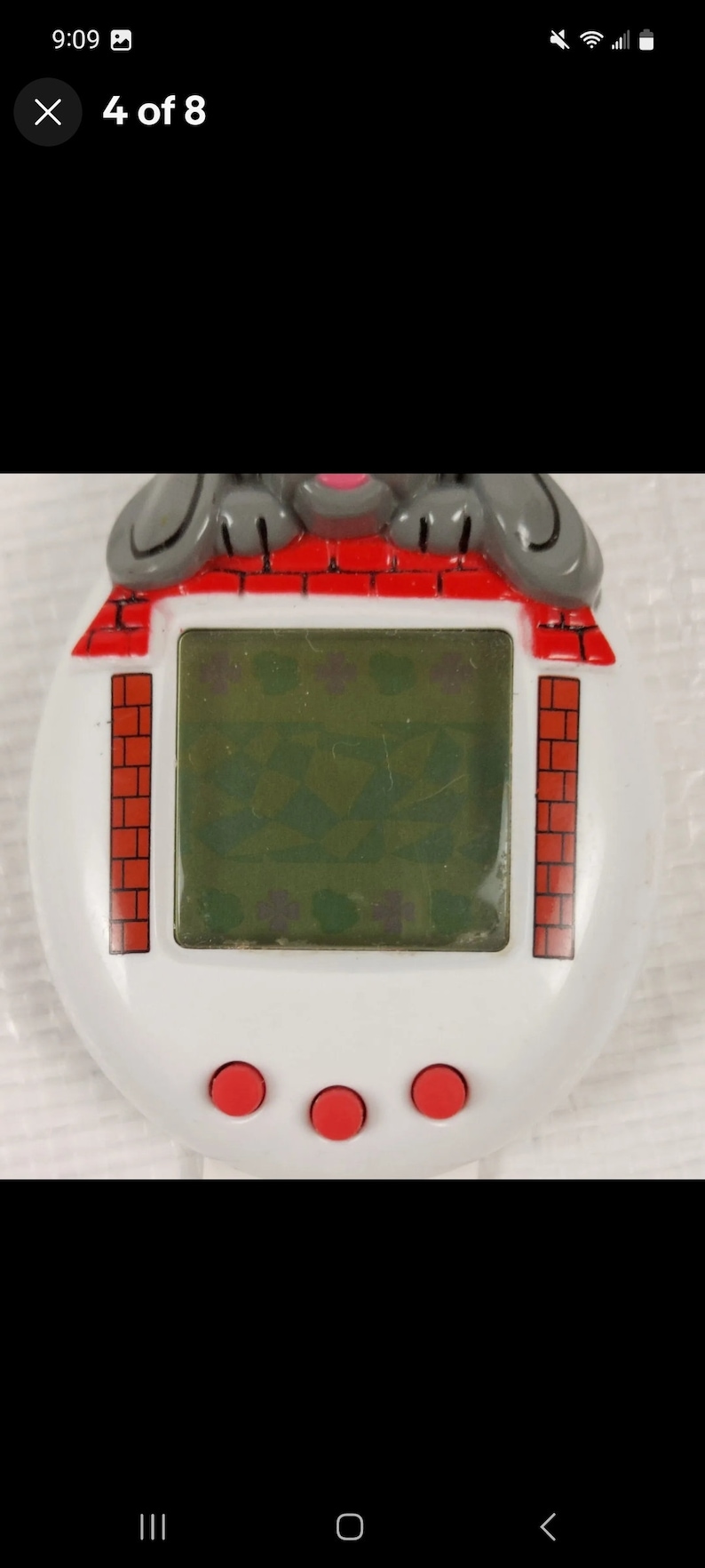K&ouml;nnte beinhalten: Ein wei&szlig;es und rotes Spielzeug aus Plastik mit einem grauen Hundegesicht oben drauf. Das Spielzeug hat einen kleinen LCD-Bildschirm und drei rote Kn&ouml;pfe. Der Bildschirm zeigt ein gr&uuml;nes und wei&szlig;es Muster.