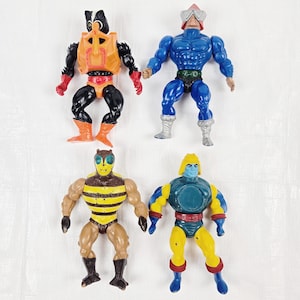 Puede incluir: Cuatro figuras de acción vintage de la línea de juguetes Masters of the Universe. Las figuras están en varias poses e incluyen una figura azul con casco, una figura amarilla con casco, una figura negra con casco y una figura marrón y amarilla con un diseño de abeja.