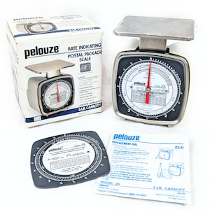 May include: A Pelouze Model Z5 postal package scale with a 5 lb. capacity, featuring a white body, a square metal platform, and a round dial with a red pointer. Includes the original box, a replacement dial, and an instruction sheet for the scale.