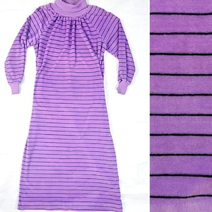 Puede incluir: Un vestido largo de manga larga, de color morado con rayas horizontales negras. El vestido tiene cuello alto y un corte holgado.