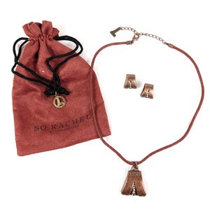 May include: A copper-toned necklace with a cord strap and a matching pair of clip-on earrings, featuring a textured triangular pendant design with a central vertical row of small beads. Includes a rust-colored drawstring pouch labeled SO RACHEL.