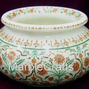 May include: A white marble decorative bowl with detailed floral inlay. The bowl has orange and green floral patterns around the rim and body. The text "Marble Crafts" is visible on the side.