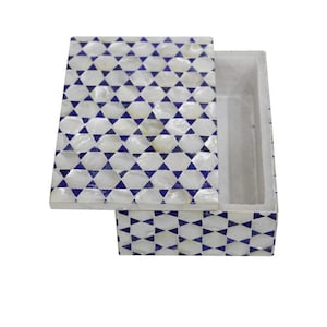 Op de afbeelding: Een rechthoekige doos met een deksel, versierd met een wit en blauw geometrisch patroon. Het deksel staat een beetje open en toont de binnenkant van de doos. De doos is waarschijnlijk gemaakt van een hard materiaal, mogelijk steen of iets dergelijks.