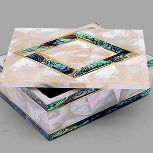 May include: A square box with a lid, featuring a mosaic of iridescent white mother-of-pearl tiles. The lid and sides are accented with a diamond-shaped border of green and blue abalone shell inlay, separated by thin gold-toned metal strips.
