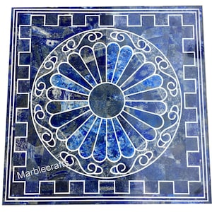 Op de afbeelding: Vierkante blauwe marmeren tafelblad met een wit bloemmotief in het midden. Het tafelblad heeft een mozaïekpatroon met een witte rand en de tekst "Marblecrafts".