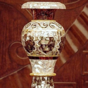 Puede incluir: Un jarrón decorativo con un diseño de mosaico. El jarrón presenta una parte superior ancha y acampanada y un cuerpo bulboso, con una base que se estrecha. El mosaico está hecho de piezas blancas y marrones iridiscentes, creando un efecto brillante. Es un artículo decorativo.