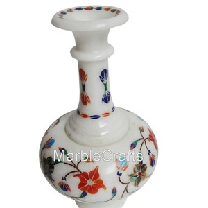 Könnte beinhalten: Eine weiße Marmorvase mit aufwendigen floralen Einlegearbeiten aus bunten Steinblütenblättern in Rot-, Blau- und Grüntönen. Die Vase hat einen schmalen Hals und einen bauchigen Körper, wobei der Text MarbleCrafts auf der Vorderseite zu sehen ist.