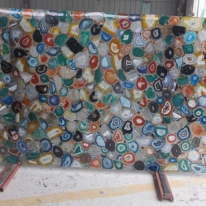 May include: A large rectangular slab composed of numerous polished agate slices in a vibrant array of colors including blue, green, red, orange, yellow, black, and white. The translucent stones are arranged in a dense mosaic pattern.