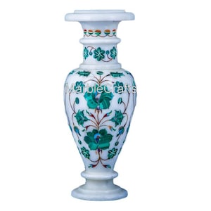 May include: White marble vase with detailed green floral inlay. The vase has a flared top and base, with the text "MarbleCrafts" on the body. The vase is a decorative item.