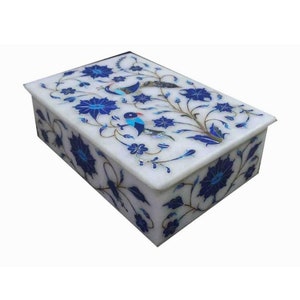 May include: A rectangular white stone box featuring intricate floral and bird inlay work in shades of deep blue, light blue, and brown. The lid and sides are decorated with detailed flower blossoms, winding vines, and two small bird figures.