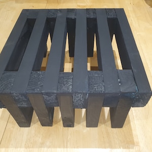 May include: Black wooden shelf unit with six open compartments. The shelf is made of thick, sturdy wood and has a rustic, industrial look.