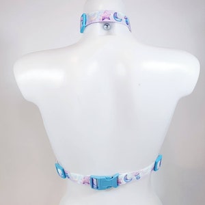 May include: A white halter top with a blue and purple moon and star print. The top has adjustable straps and a plastic buckle closure in the back.