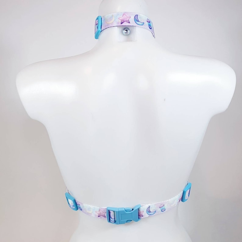 May include: A white halter top with a blue and purple moon and star print. The top has adjustable straps and a plastic buckle closure in the back.