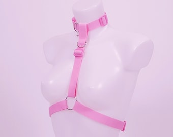 May include: Pink adjustable harness with a choker and metal rings. The harness is made of soft, stretchy fabric and is designed to fit comfortably around the body.