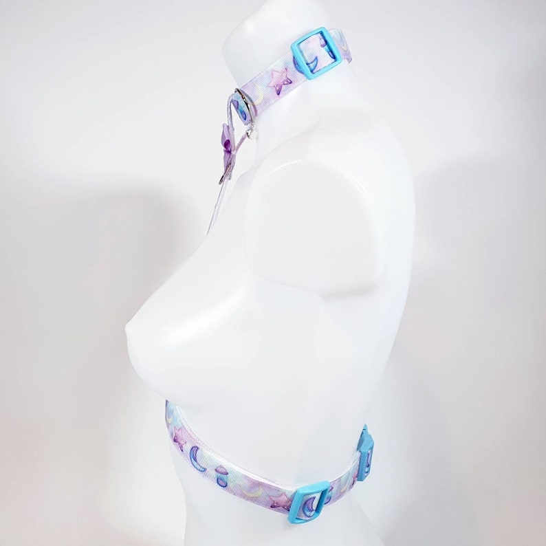 May include: A light blue choker with a white and purple moon and star pattern. The choker has two adjustable buckles.